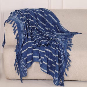 Puede incluir: Manta estampada azul y blanca con flecos, sobre un sof&aacute; beige. La manta presenta un dise&ntilde;o en zigzag repetido y est&aacute; hecha de un material suave y tejido. Los flecos est&aacute;n a lo largo de los bordes de la manta.