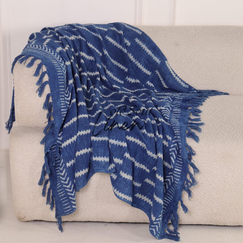 Puede incluir: Manta estampada azul y blanca con flecos, sobre un sof&aacute; beige. La manta presenta un dise&ntilde;o en zigzag repetido y est&aacute; hecha de un material suave y tejido. Los flecos est&aacute;n a lo largo de los bordes de la manta.