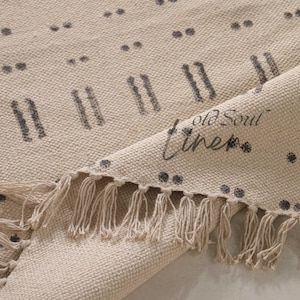 May include: A cream-colored rug with a black and white geometric pattern. The rug has a fringe border and is made of cotton.