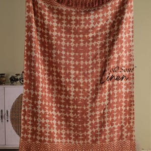 May include: A terracotta-colored linen throw blanket with a repeating floral pattern in a lighter beige hue. The blanket has a fringed edge and a geometric border design. The text "old soul linen" is visible on the blanket.