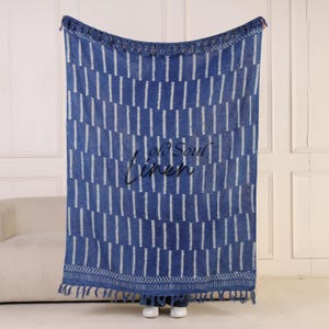 Puede incluir: Manta de lino con estampado azul y blanco con ribete de flecos. La manta presenta rayas blancas verticales sobre un fondo azul. Las palabras "Old Soul Linen" est&aacute;n bordadas en negro en la parte delantera.