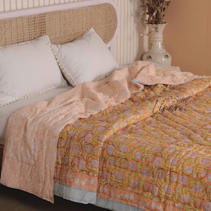 Könnte beinhalten: Ein Bett mit weißen Kissen und einer floral gemusterten Steppdecke. Die Steppdecke zeigt ein lebhaftes orange-grünes Blumenmuster mit einer hellpfirsichfarbenen Rückseite. Das Bett steht vor einem hellfarbigen Kopfteil.
