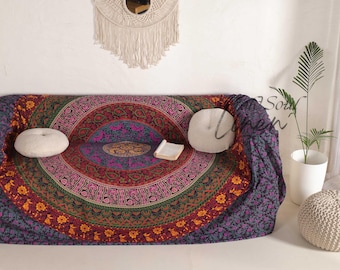 Puede incluir: Un tapiz mandala de color morado oscuro y rojo con intrincados patrones florales y un acento dorado. El tapiz está drapeado sobre un sofá con dos almohadas blancas.