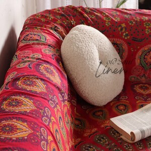 Puede incluir: Una manta de tiro con estampado paisley rojo y blanco con una almohada redonda blanca en un sof&aacute;. El texto "old soul linen" es visible en la almohada.
