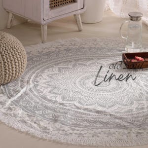May include: A white and gray round mandala rug with a fringe border. The rug is on a light wood floor.