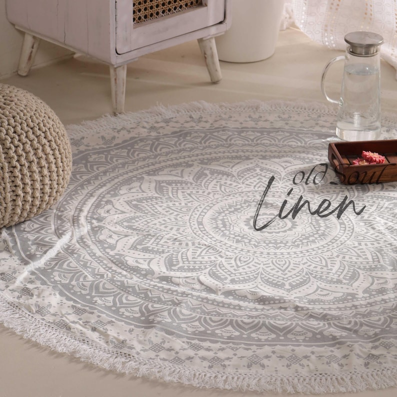 May include: A white and gray round mandala rug with a fringe border. The rug is on a light wood floor.