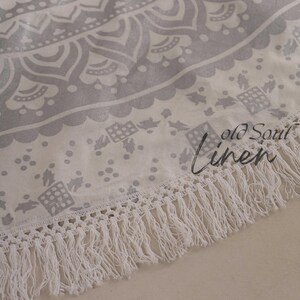 May include: A white round tapestry with a gray mandala design and white fringe. The tapestry has the text "Old Soul Linen" printed on it.