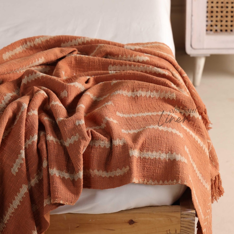Handwoven terracotta cotton throw blanket with subtle geometric patterns and tassel edges, displayed as boho bedroom decor.