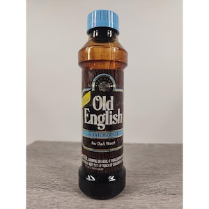 May include: A bottle of Old English Scratch Cover for dark wood. The bottle has a brown, wood-grain design with a blue cap and black base. The label reads "Old English" and "Scratch Cover".
