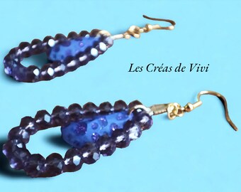 Könnte beinhalten: Ein Paar violette und goldene Ohrringe mit einer blauen Perle in der Mitte. Die Ohrringe bestehen aus kleinen Perlen und haben einen Hakenverschluss. Der Text "Les Créas de Vivi" ist im Bild sichtbar.