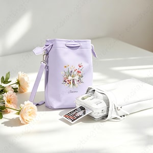 May include: A light purple bucket bag with a floral design and a white bag with a camera inside. The bucket bag has a shoulder strap and the text "Jomna" below the floral design. The white bag also has a shoulder strap.