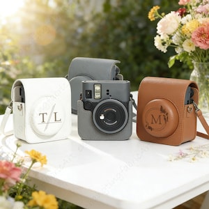May include: Three camera cases in white, gray, and brown, each with a camera inside. The white case has the initials "T/L" engraved, and the brown case has the letter "M" engraved. All cases have shoulder straps.