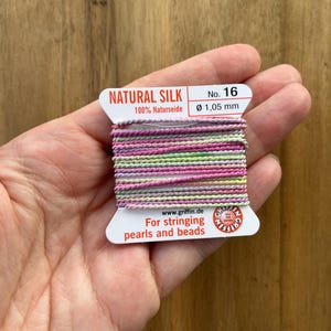 May include: A spool of natural silk thread, No. 16, with a diameter of 1.05 mm. The thread is a mix of pink, purple, and green hues. The label reads "NATURAL SILK" and "For stringing pearls and beads."