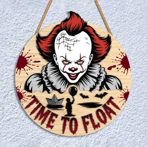 May include: Round wooden sign featuring a menacing clown with red hair and makeup, surrounded by blood splatters. The sign reads "TIME TO FLOAT" in red lettering, with a paper boat, a child holding a balloon, and bats. A rope is attached for hanging.