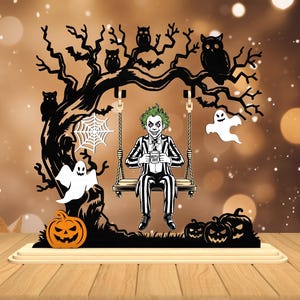 May include: A Halloween-themed decorative piece featuring a black tree with owls, bats, and a spiderweb. A figure in a striped suit and green hair is seated on a swing, holding a mug that says "Beetle Juice". Pumpkins and ghosts complete the spooky scene.