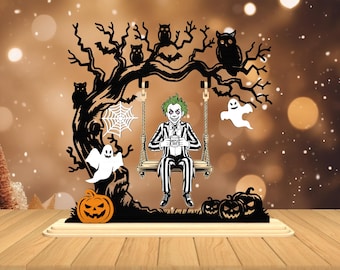 Può includere: Decorazione a tema Halloween con un albero nero con gufi, pipistrelli e una ragnatela. Una figura in abito a righe e capelli verdi è seduta su un'altalena, con in mano una tazza con la scritta "Beetle Juice". Zucca e fantasmi completano la scena.