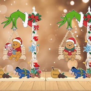 May include: Christmas-themed wooden decorations featuring Winnie the Pooh characters. One shows Pooh and Piglet on a swing, the other shows Pooh with a mug. Both have a Grinch hand, a pole with lights, and Eeyore pulling a cart.