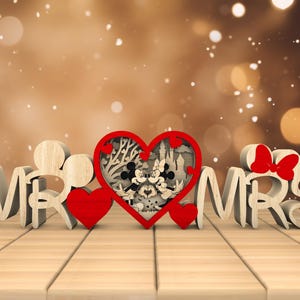 May include: Wooden "Mr." and "Mrs." sign with a red heart in the middle. The heart has a cutout design of Mickey and Minnie Mouse in front of a castle.