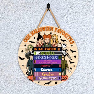 May include: Circular wooden sign featuring the text "OUR HALLOWEEN FAVORITES" and Halloween-themed illustrations. The sign depicts characters and titles from popular Halloween films, including Beetlejuice and Hocus Pocus.