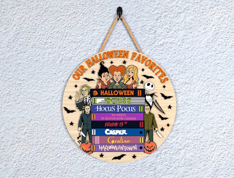 May include: Circular wooden sign featuring the text "OUR HALLOWEEN FAVORITES" and Halloween-themed illustrations. The sign depicts characters and titles from popular Halloween films, including Beetlejuice and Hocus Pocus.
