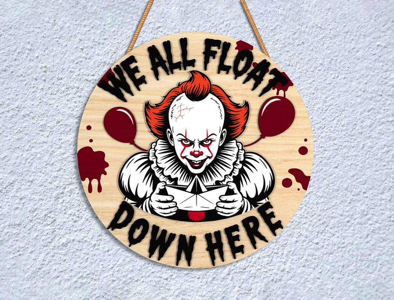May include: Round wooden sign featuring a menacing clown with red hair and makeup, holding a paper boat. The sign reads "WE ALL FLOAT DOWN HERE" in black letters, with red balloon and blood splatter accents. A rope is attached for hanging.