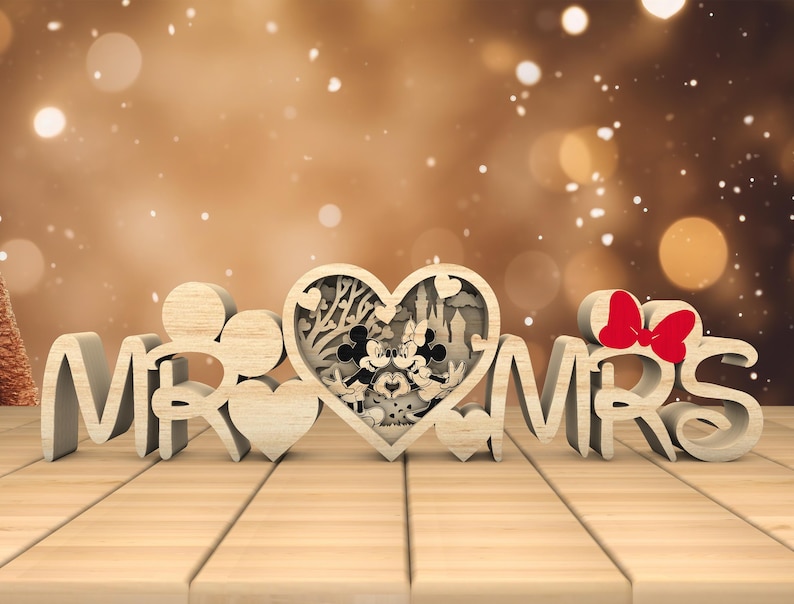 May include: Wooden "Mr. & Mrs." sign with a heart-shaped cutout featuring a silhouette of Mickey and Minnie Mouse. The heart is surrounded by a floral design.