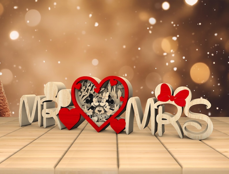 May include: Wooden "Mr. & Mrs." sign with a red heart in the centre featuring a Mickey Mouse and Minnie Mouse design. The heart is surrounded by a decorative floral pattern.