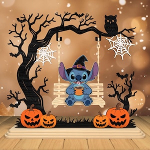 May include: A Halloween-themed wooden decoration featuring a cartoon character wearing a witch hat, sitting on a swing. The scene includes carved pumpkins, trees, an owl, and spiderwebs, all set against a blurred background.