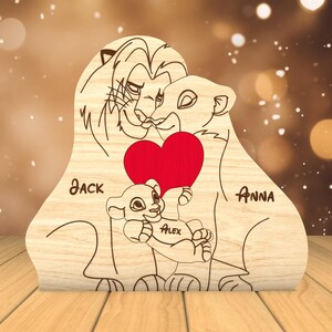 K&ouml;nnte beinhalten: Holzausschnitt einer L&ouml;wenfamilie mit einem roten Herzen. Die L&ouml;weneltern hei&szlig;en Jack und Anna, und ihr Junges hei&szlig;t Alex.