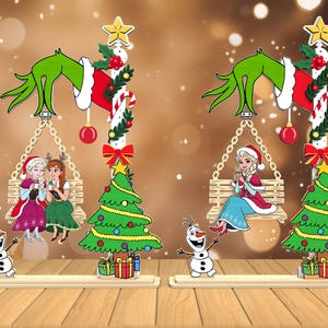 May include: Christmas-themed wooden decoration featuring a Grinch hand, a swing with cartoon characters, a Christmas tree, and a snowman. The Grinch's hand holds a swing with two cartoon characters. A Christmas tree and snowman are also present.