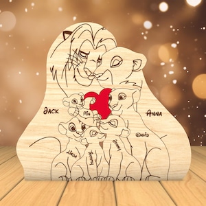 K&ouml;nnte beinhalten: Ein Holzausschnitt einer L&ouml;wenfamilie mit einem roten Herzen in der Mitte. Die Eltern sind mit "Jack" und "Anna" beschriftet und die Kinder mit "Mia", "Linda", "Tommy", "Benny" und "David".