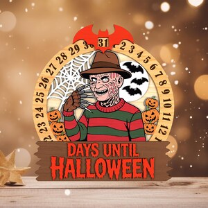 May include: A wooden Halloween countdown calendar featuring a character with a hat and striped sweater. The calendar has a circular design with numbers, pumpkins, bats, and a spiderweb. The text "DAYS UNTIL HALLOWEEN" is displayed on a wooden sign.