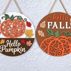 May include: Two round wooden signs with fall themes. One says "Hello Pumpkin" with an orange pumpkin and colorful leaves. The other says "Hello Fall" with an orange pumpkin and leaves. Both have a rope for hanging.