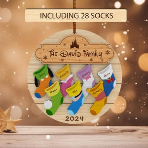 Könnte beinhalten: Ein hölzerner Weihnachtsbaumschmuck mit einem Disney-Schloss-Design und dem Text "The David Family", umgeben von 8 bunten Strümpfen mit Namen. Der Schmuck enthält auch den Text "INCLUDING 28 SOCKS" und "2024".