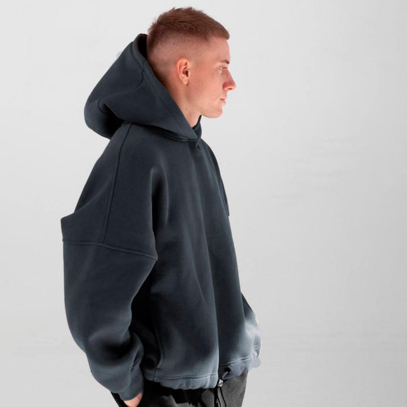 May include: A dark gray hoodie with a large hood and a drawstring at the bottom hem. The hoodie has a relaxed fit and long sleeves. The fabric appears to be a soft, medium-weight material. The overall style is casual and comfortable.