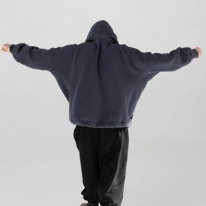 May include: A navy blue hooded sweatshirt with a relaxed fit, featuring a drawstring hem and a hood. The person is wearing black sweatpants. The sweatshirt's sleeves are extended, and the person is facing away from the camera.