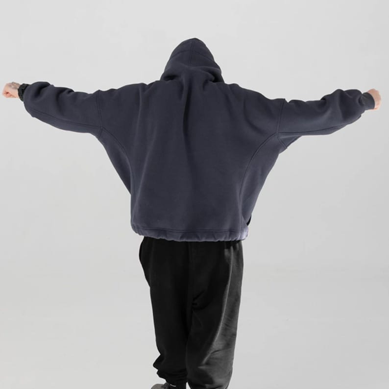 May include: A navy blue hooded sweatshirt with a relaxed fit, featuring a drawstring hem and a hood. The person is wearing black sweatpants. The sweatshirt's sleeves are extended, and the person is facing away from the camera.