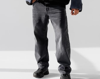 May include: A person wearing dark gray jeans and black shoes. The jeans have a relaxed fit and are cuffed at the ankles.