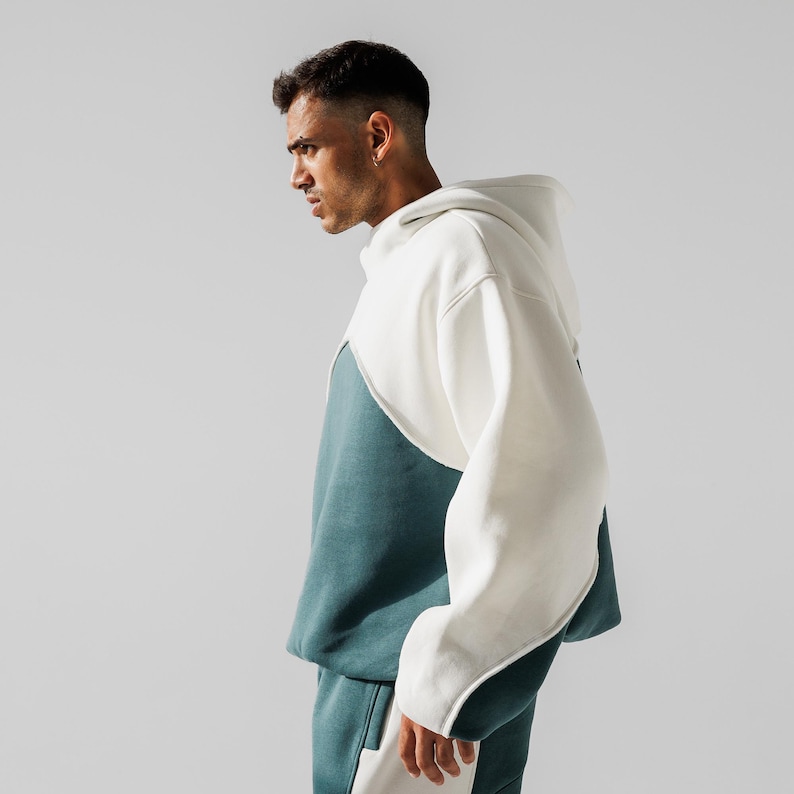 May include: A two-tone hoodie and matching sweatpants set. The hoodie is white and teal, with a unique design. The sweatpants have a white stripe down the side. The outfit is made of a soft, comfortable material.