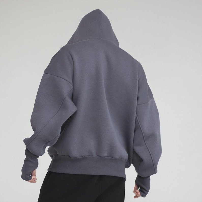 May include: A gray hooded sweatshirt with a relaxed fit. The sweatshirt features a large hood, long sleeves with thumbhole cuffs, and a ribbed hem. The back view shows the garment's oversized silhouette and solid color.