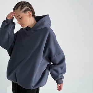 May include: A dark blue oversized hoodie with a large hood and long sleeves. The hoodie has a relaxed fit and ribbed cuffs. The fabric appears to be a soft, comfortable material. The hoodie is a solid color, with no visible graphics or patterns.