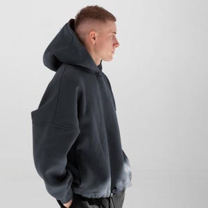 May include: A dark gray hoodie with a large hood and a relaxed fit. The bottom of the hoodie has a faded, lighter gray color. The hoodie is made of a soft material and has a drawstring at the bottom.