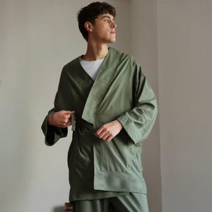 May include: An olive green kimono-style robe with wide sleeves and a matching belt. The robe is made of a soft, flowing fabric and is worn over a white t-shirt. The outfit is part of a loungewear set.