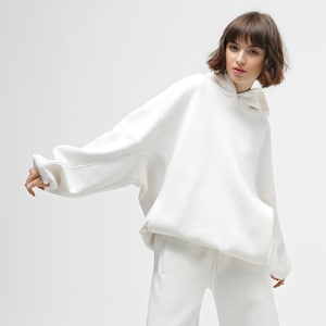 May include: A white hoodie with a matching pair of sweatpants. The hoodie has a drawstring hood and a kangaroo pocket. The outfit is made of a soft, comfortable material. The model is wearing the outfit.