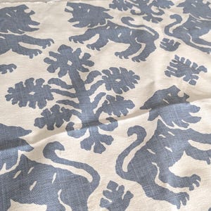 May include: A white fabric with a repeating pattern of blue stylized lions and floral designs. The fabric has a subtle texture.