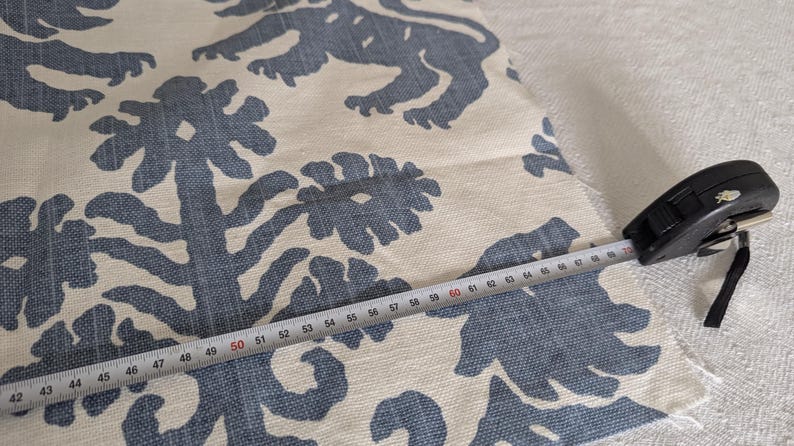 May include: Close-up of a white fabric with a blue floral pattern. A measuring tape is placed on the fabric, showing a measurement of 50 inches.