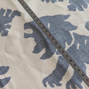 May include: A white fabric with a blue pattern of stylized animal shapes. A metal ruler is placed diagonally across the fabric, with the numbers 49 through 61 visible.
