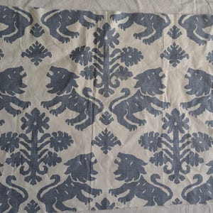 May include: A white fabric with a repeating pattern of blue stylized lions and floral designs. The fabric has a slightly textured surface.