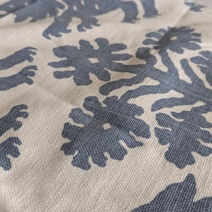 May include: A close-up of a beige fabric with a repeating pattern of dark blue stylized lions and floral designs.