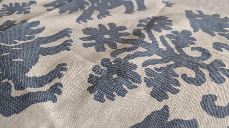 May include: A close-up of a beige fabric with a repeating pattern of dark blue stylized lions and floral designs.